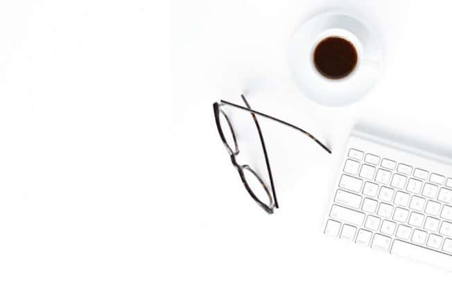 Glasses, cup of coffee and keyboard sitting on white table