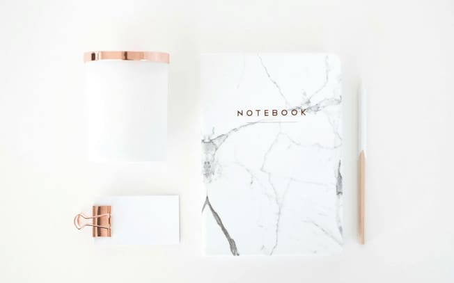 Marble notebook beside a pad of paper with a gold paper clip