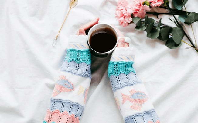 Hands holding a mug of coffee with flowers laying beside