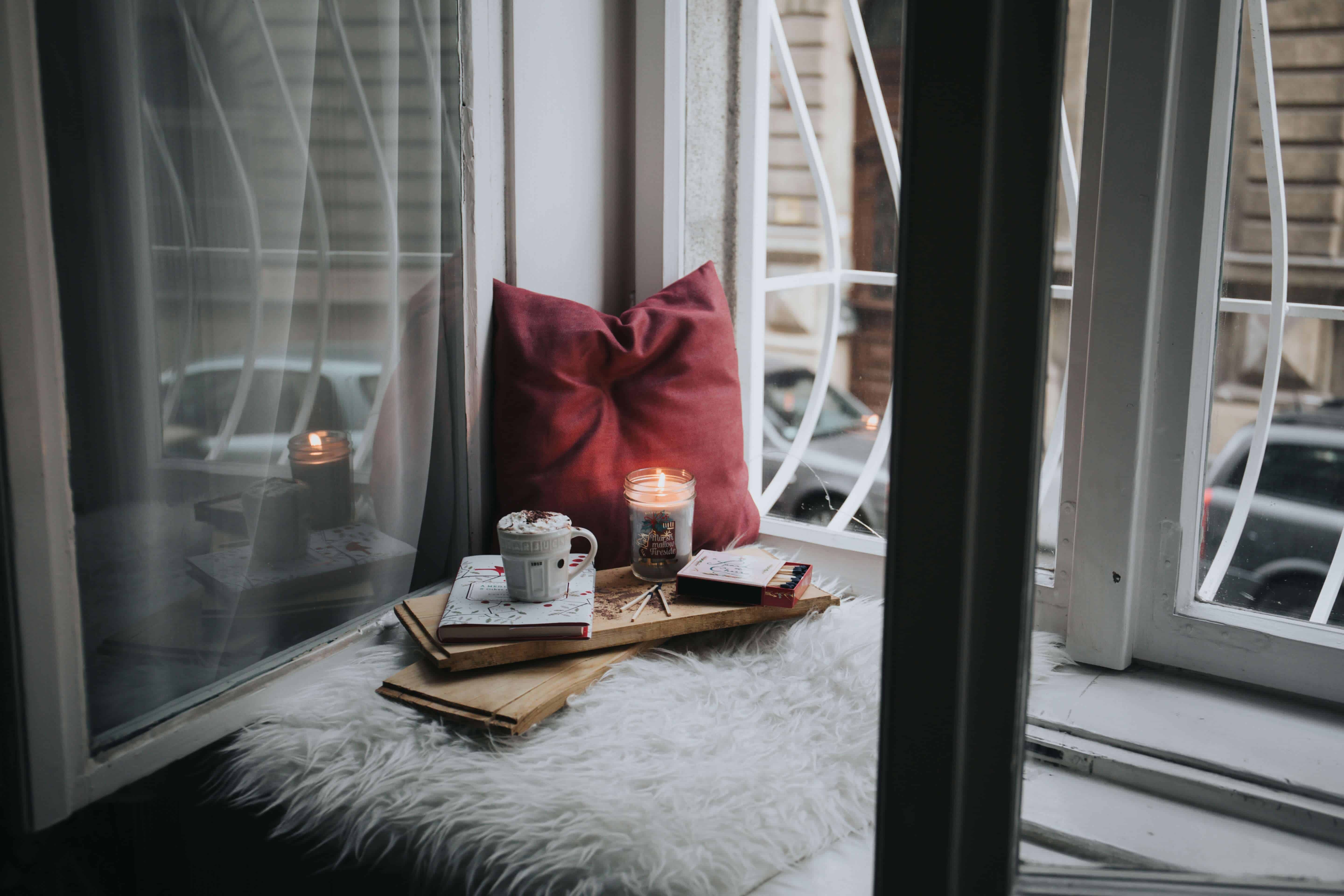 A hygge spot by the window with candles, tea and pillows.