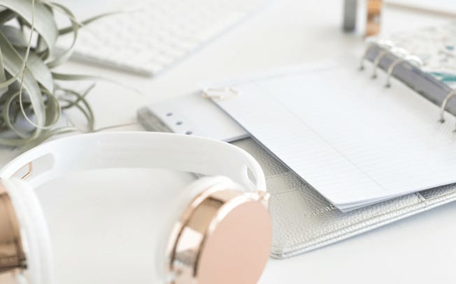 Gold headphones beside a notepad and a green plant