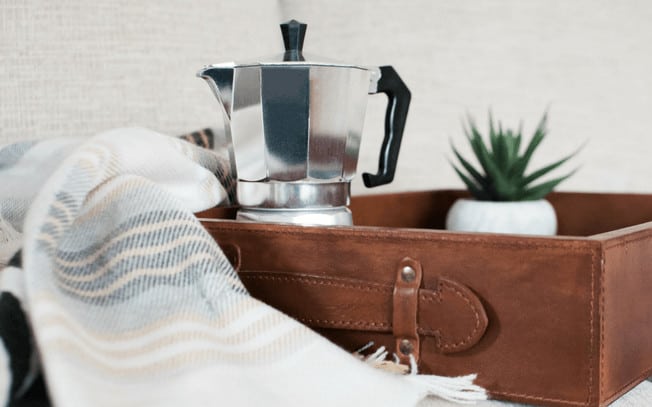 A silver coffee maker in a brown box, beside a blanket