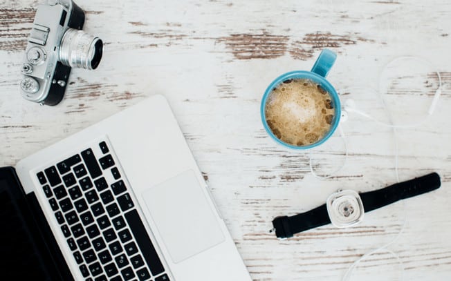 Styled photo of a watch, camera, laptop headphones and cup of coffee