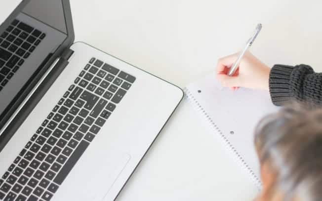 Person writing on paper with laptop