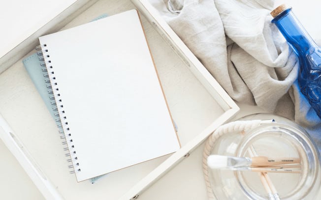 Styled photo of notebook, paintbrushes in jar, blanket and blue bottle