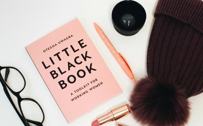 A flatlay of a book, lipstick, toque, pen and glasses