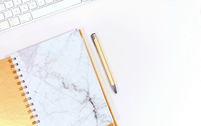 Marble notebook beside gold pen on white surface