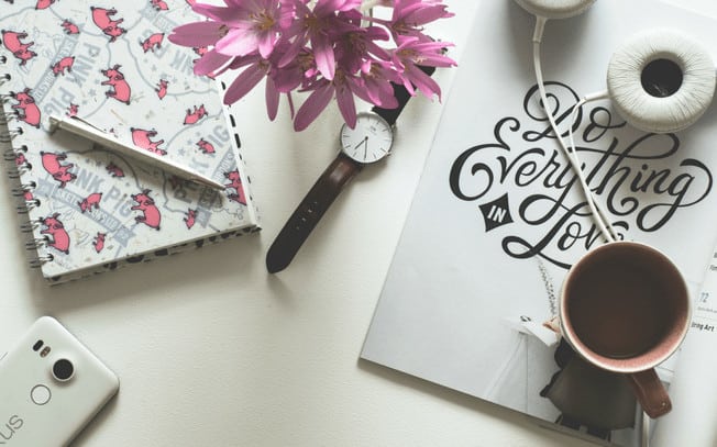 Stylized photo of watch, headphones, coffee, notepad, pen and flowers