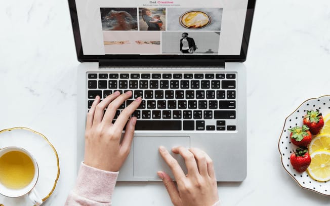 Girl typing with hands on a laptop with tea and fruit on the side