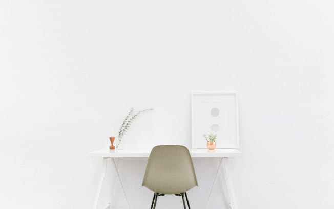A desk infront of a white wall with a photo frame and a plant