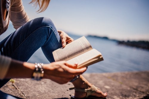 A girl reading a book by the water