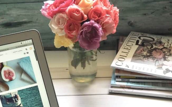 Flowers beside a stack of magazines and a laptop