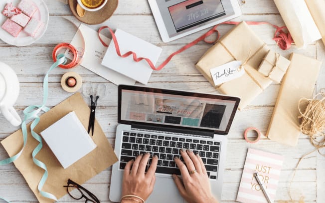 A laptop with hands typing and boxes and ribbons scattered around