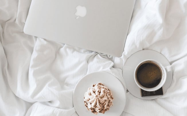 A laptop, pastry and cup of coffee placed on a bed