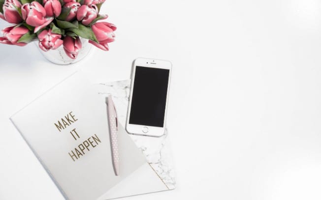 an iphone beside flowers and a pen with paper