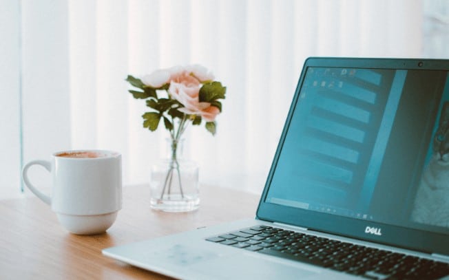 Pink flowers beside a laptop and cup of coffee on a desk