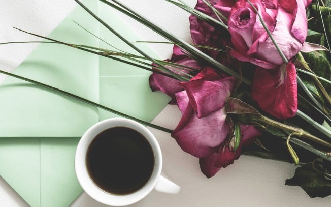 flowers beside a cup of coffee and green envelope