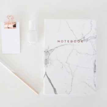 Notebook, pen, paper and nail polish on a white desk