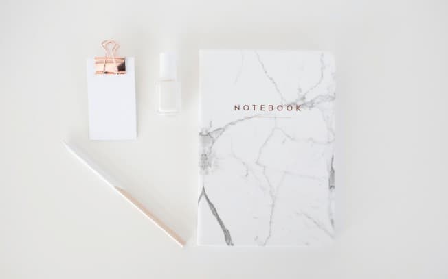 Notebook, pen, paper and nail polish on a white desk