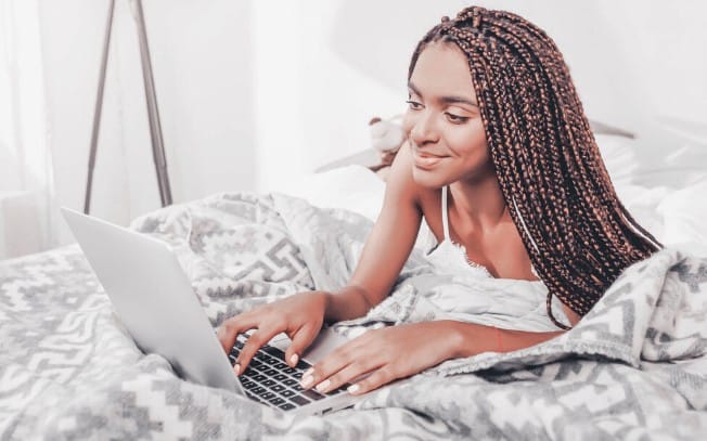 Woman laying on bed while on her laptop