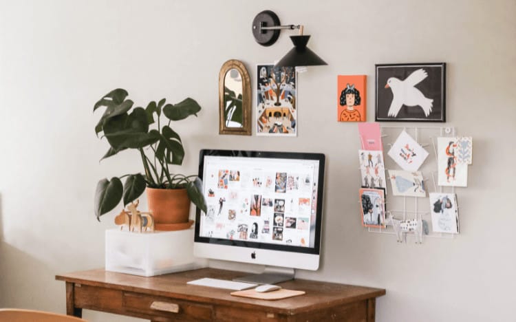 A desk with a plant beside it and artwork on the wall behind a computer.