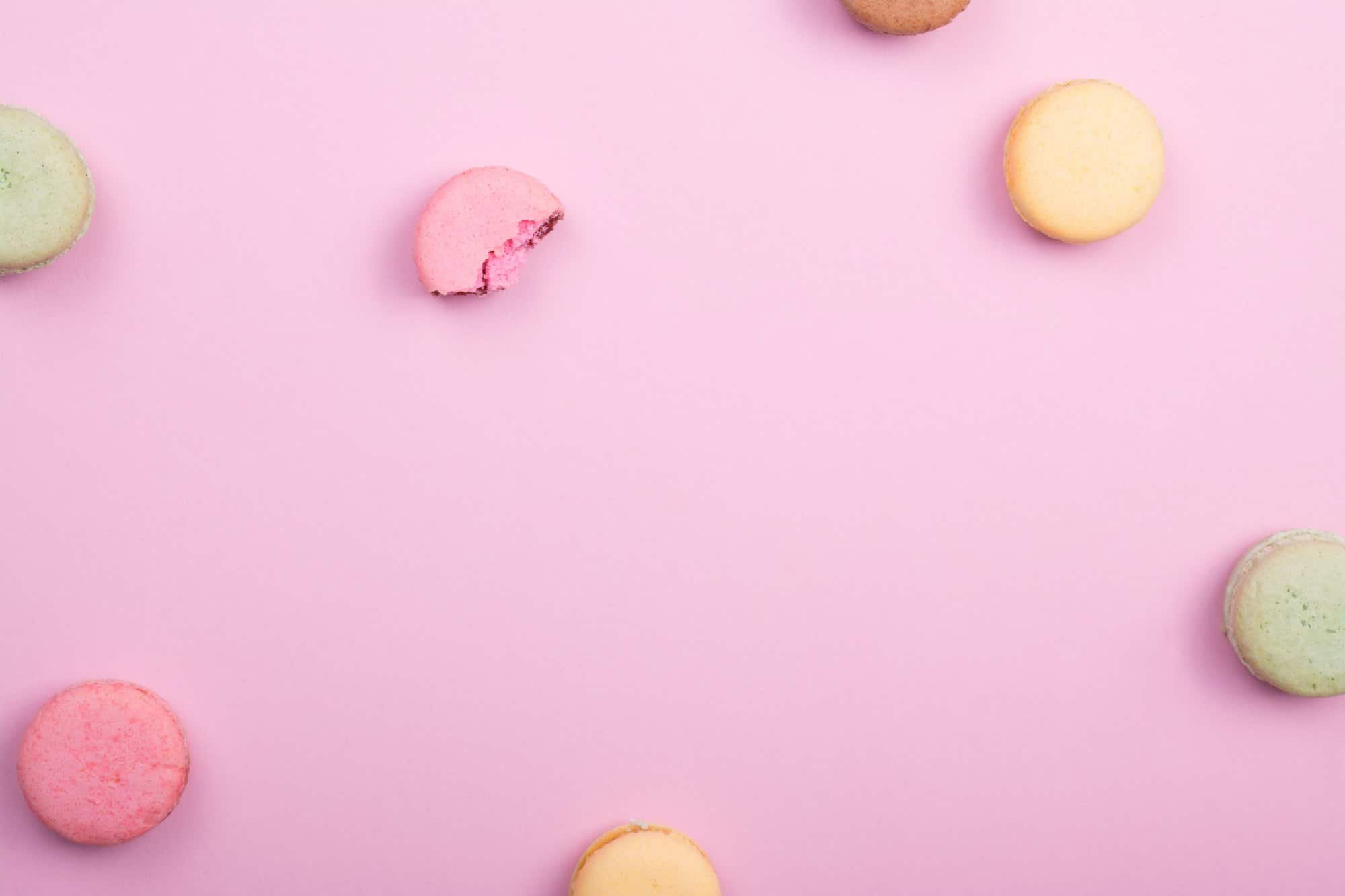 multiple macarons scattered on a pink background
