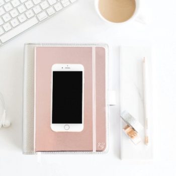 A styled photo of a cellphone on top of a book, sitting beside a keyboard