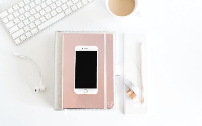 A styled photo of a cellphone on top of a book, sitting beside a keyboard