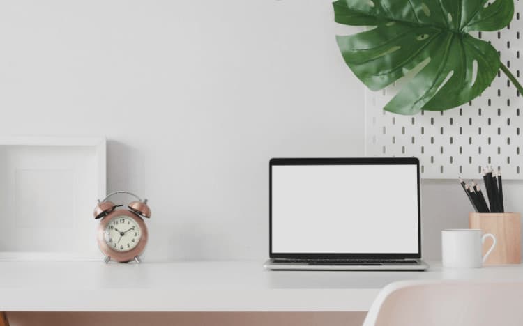 Laptop siting on a desk beside a plant and a clock.