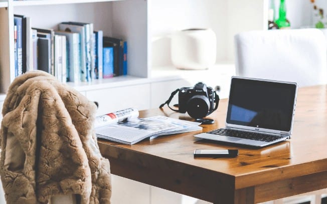 A home office with a laptop, camera and magazine on a wood table