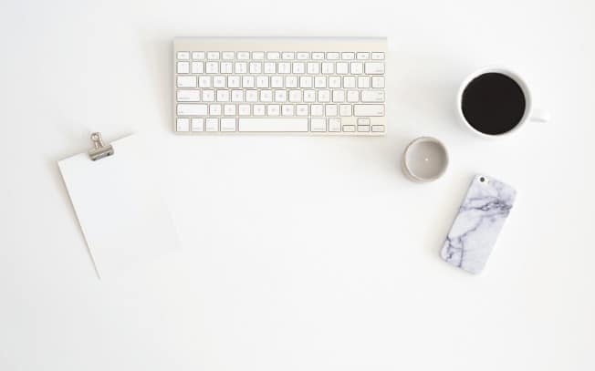 Birdseye view of a computer keyboard, coffee, notepad and phone