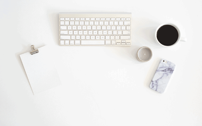 A styled stock photo of a keyboard, a cup of coffee, a notepad and a cell phone all on a desk.