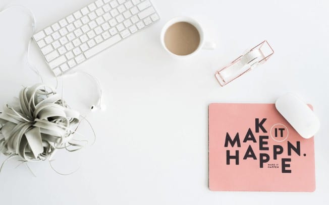 A styled photo with a coffee, a roll of tape, a mouse pad and a green plant